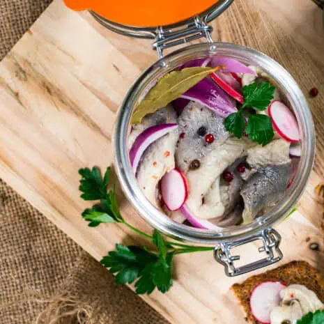 Pickled Marinated Herring with Spices, Radish and Red Onion on Wooden Background. Selective focus.