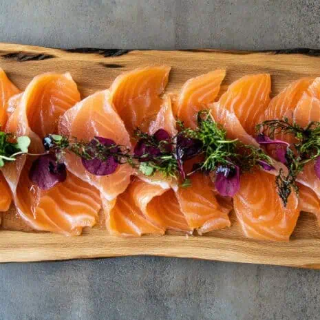 A top view of a wooden board adorned with thin slices of smoked salmon, highlighting the dish's vibrant colors and textures